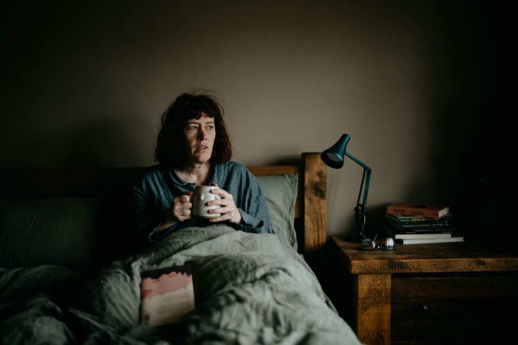 Tired woman sitting awake on the edge of her bed at night