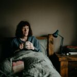 Tired woman sitting awake on the edge of her bed at night