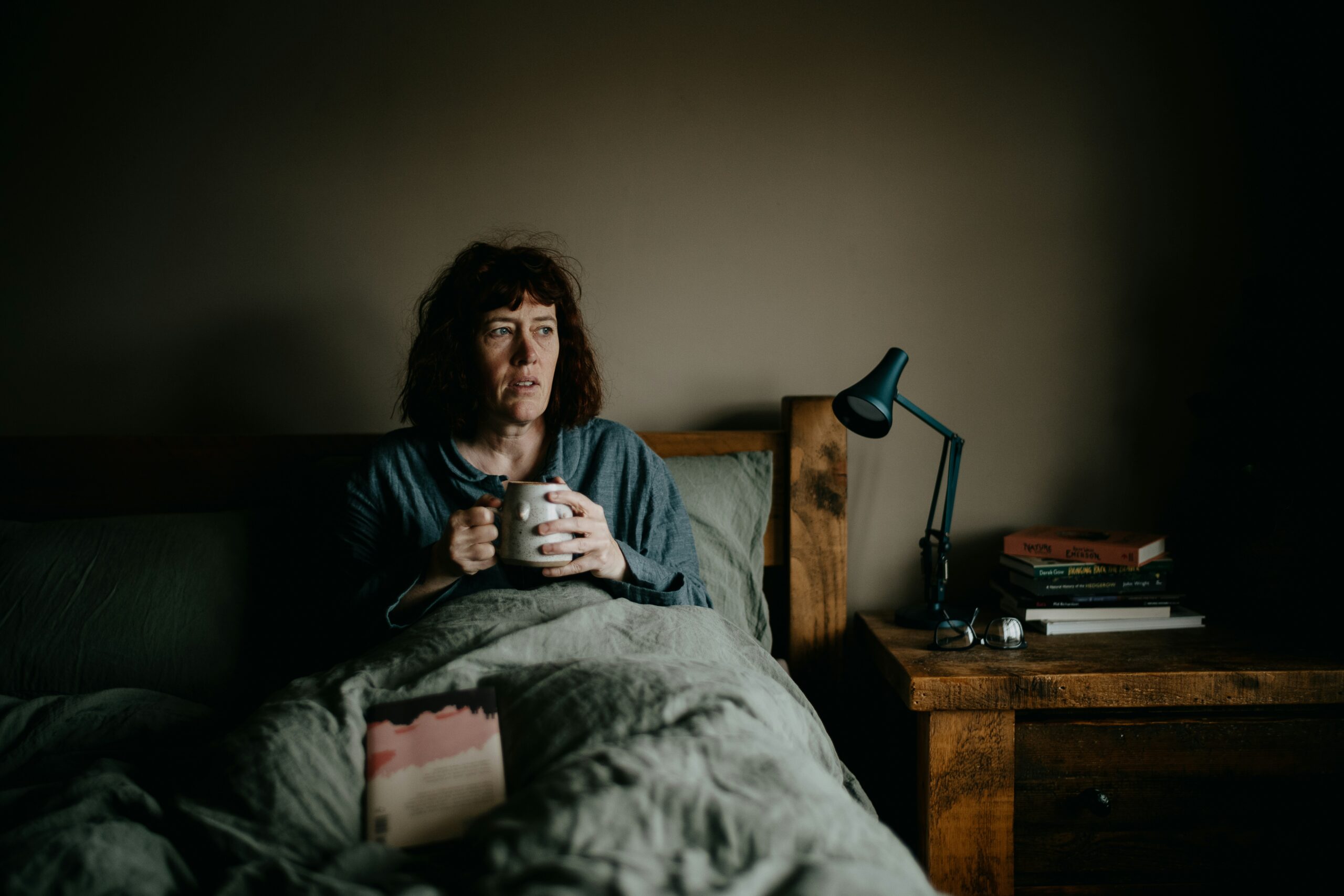 Tired woman sitting awake on the edge of her bed at night